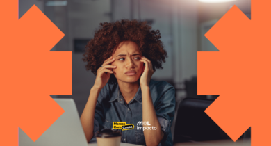 Imagem mostra mulher com cabelos black soltos e vestindo blusa jeans com expressão preocupada diante de tela de computador